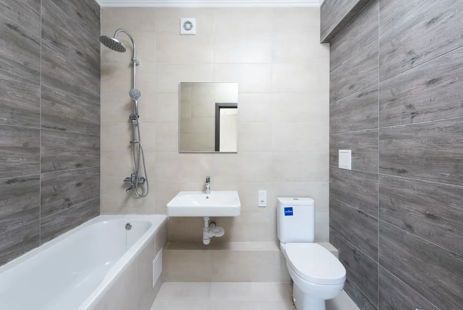 Vue d’en haut, une employée de ménage anonyme portant des gants en caoutchouc jaunes pulvérise un produit nettoyant sur un robinet d’eau chromé dans une salle de bain
